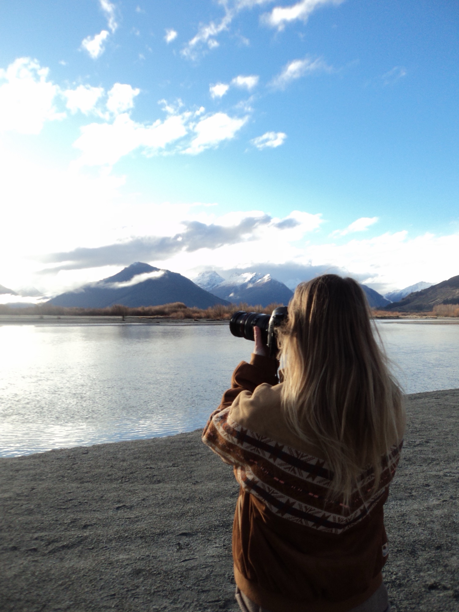 Madelene photographing a mountain lake in New Zealand, camera raised