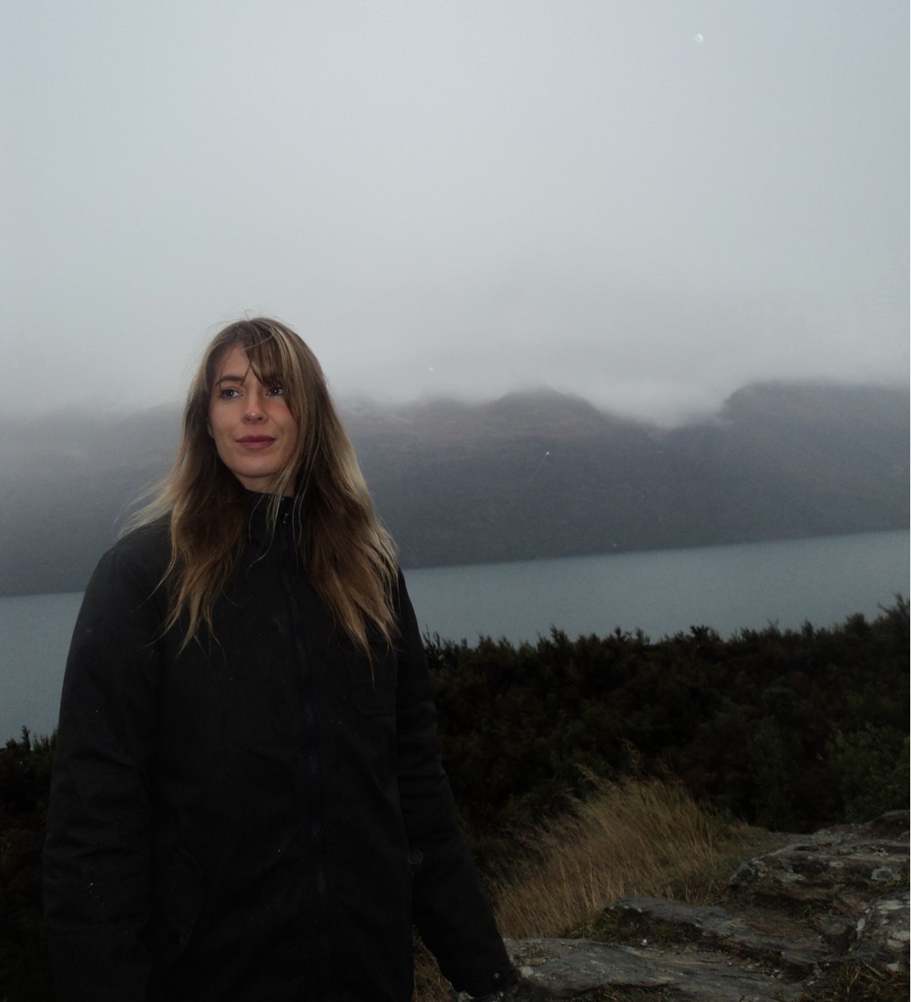 Madelene Belinki standing before a misty mountain lake, hair blowing in the wind
